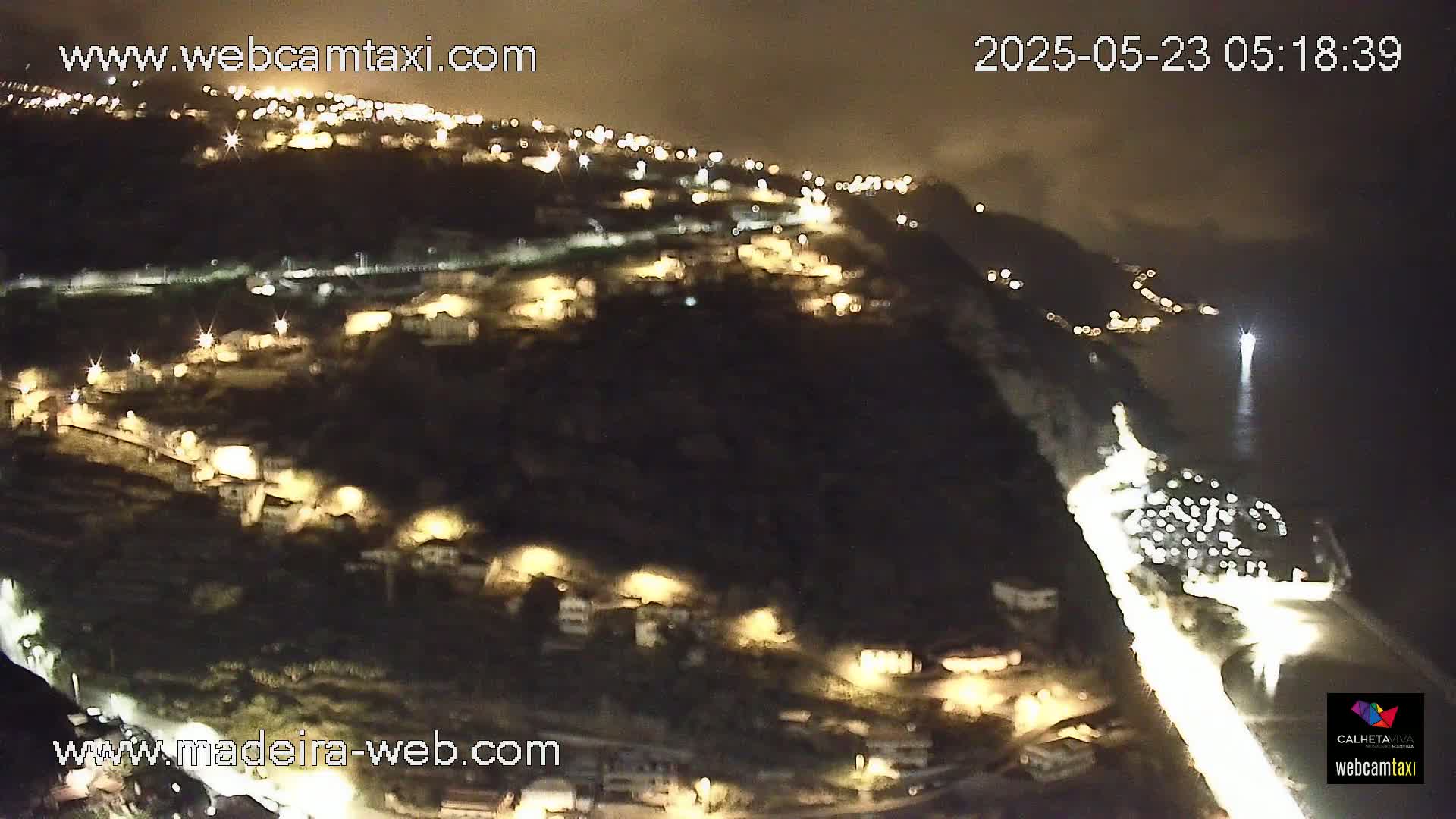 A nighttime, aerial view of a coastal town illuminated by streetlights, with a dark ocean visible in the background.
