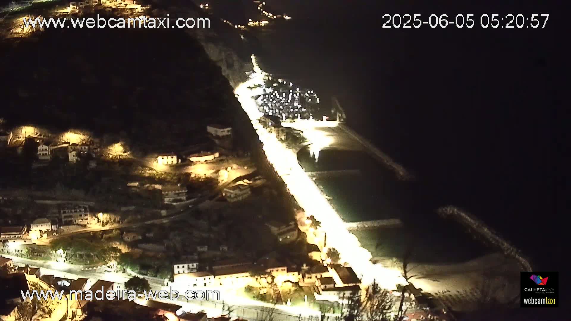 A brightly lit coastal road winds through a town at night, alongside a dark body of water.