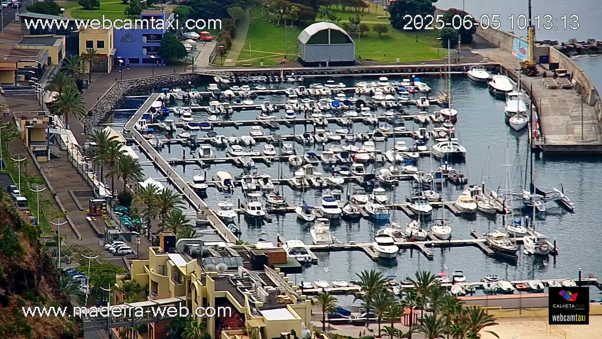 A marina filled with numerous boats and yachts is viewed from above on a partly sunny day.