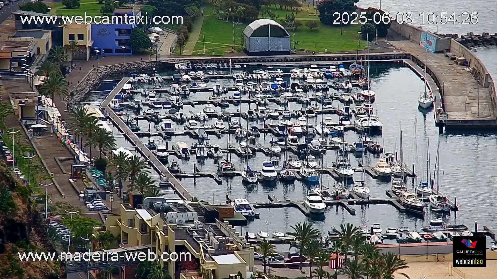 A marina filled with numerous boats and yachts is shown on a partly sunny day.
