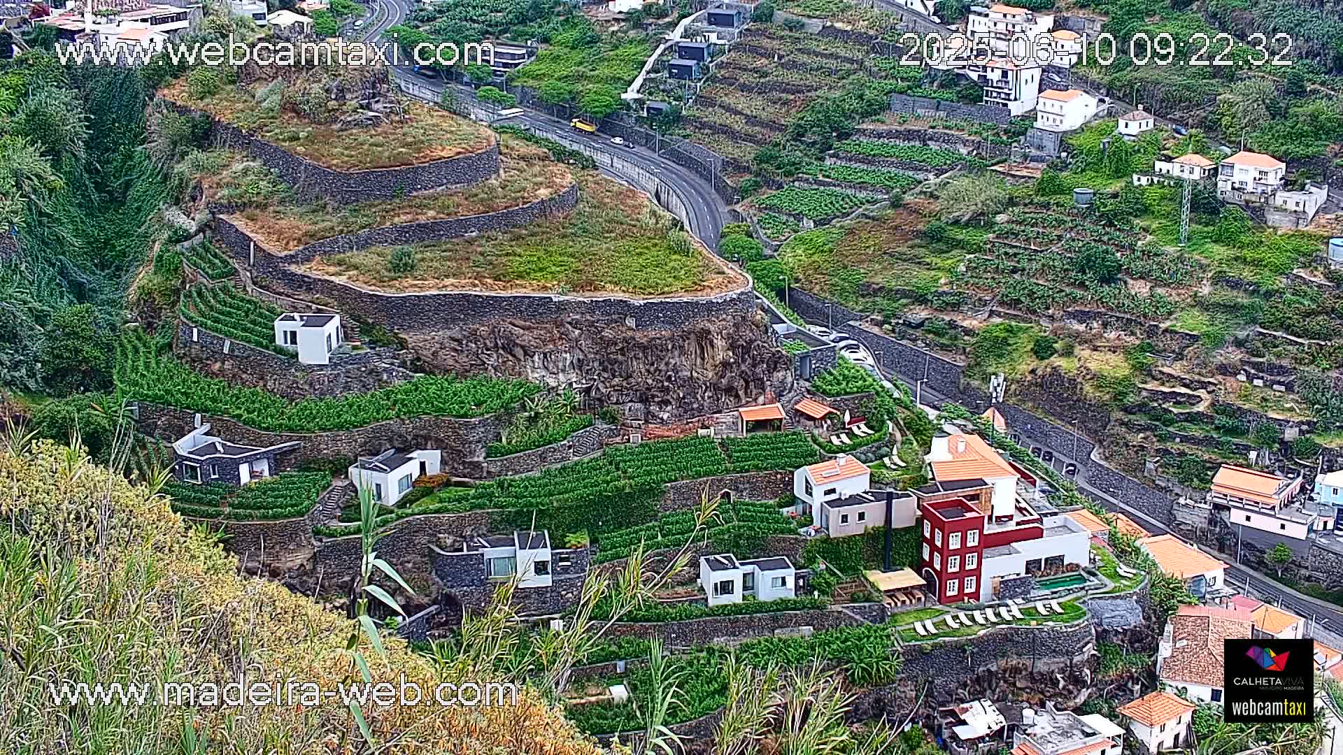 A hillside village with terraced gardens and houses overlooks a winding road.