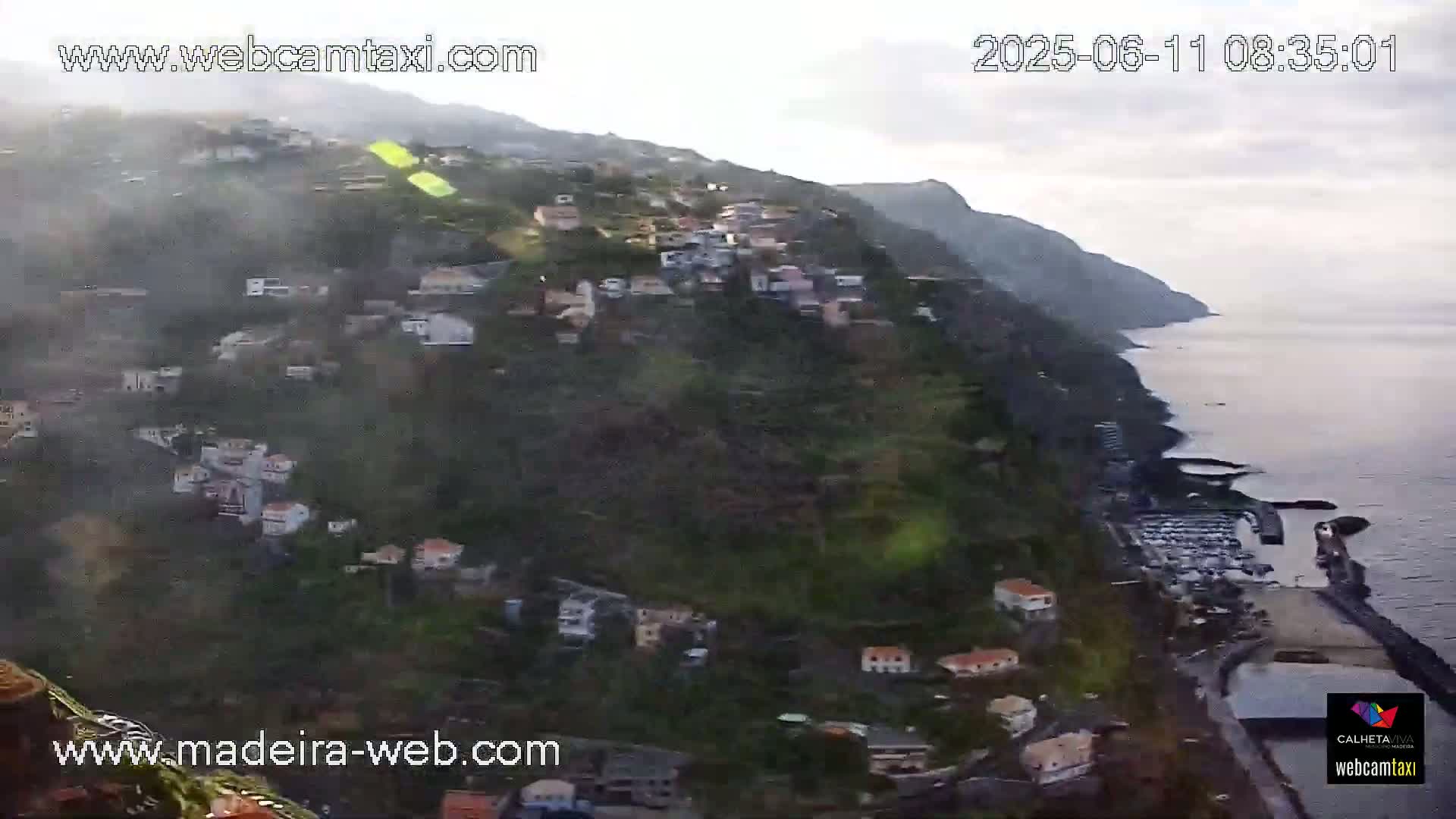 A hazy, coastal village clings to a steep hillside overlooking a calm ocean.