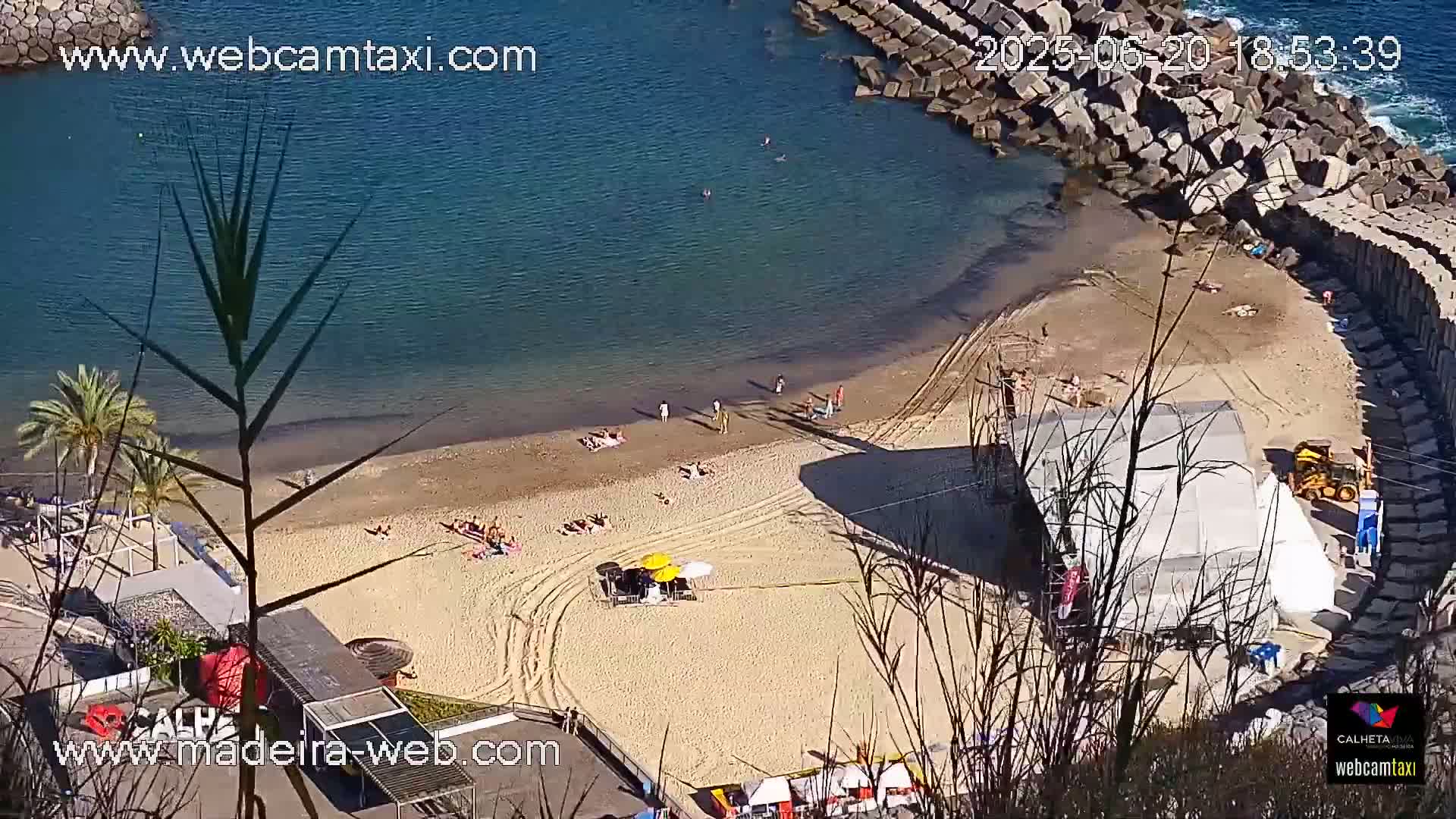 A sandy beach with several people sunbathing and swimming in a calm, clear blue ocean on a sunny day.
