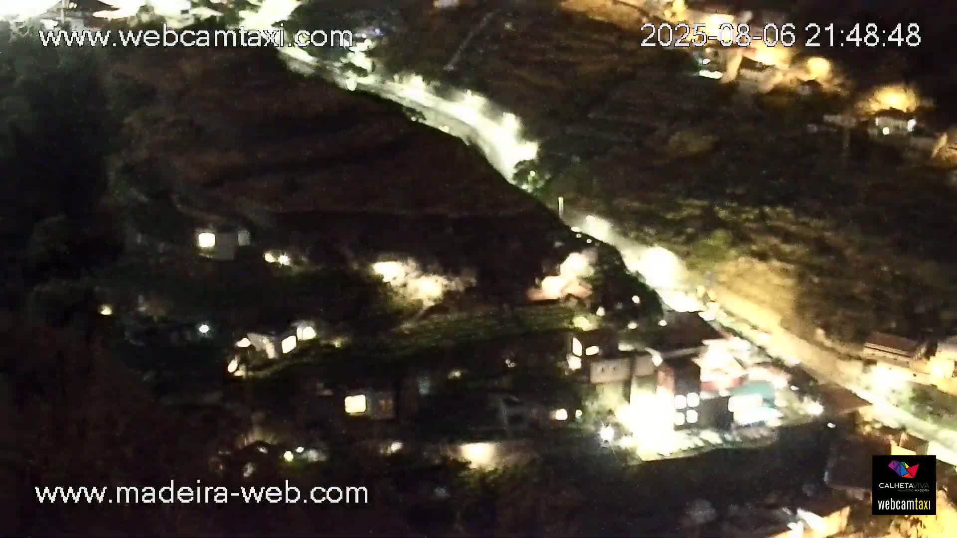 A nighttime, high-angle view shows a road winding through a dark, hilly landscape with scattered lights from buildings below.