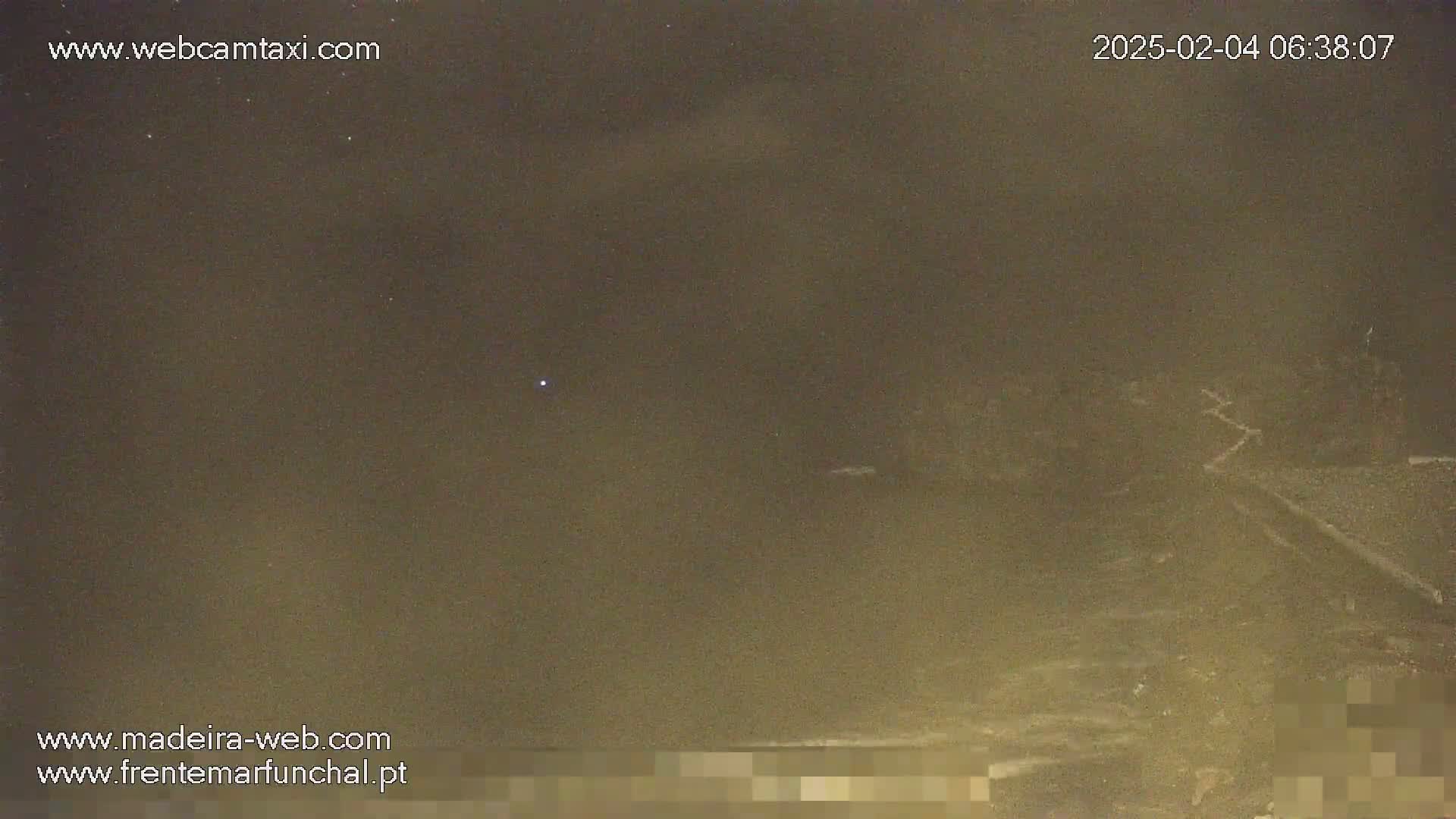 A hazy, dark night scene shows a dimly lit, possibly coastal area with faint lights in the distance.