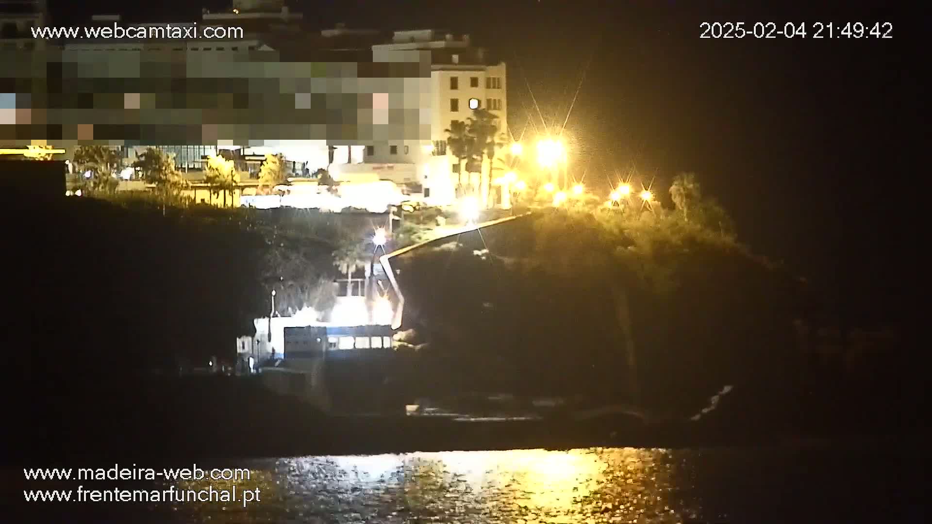 A nighttime view of a waterfront area with buildings illuminated by streetlights, reflecting on calm water.