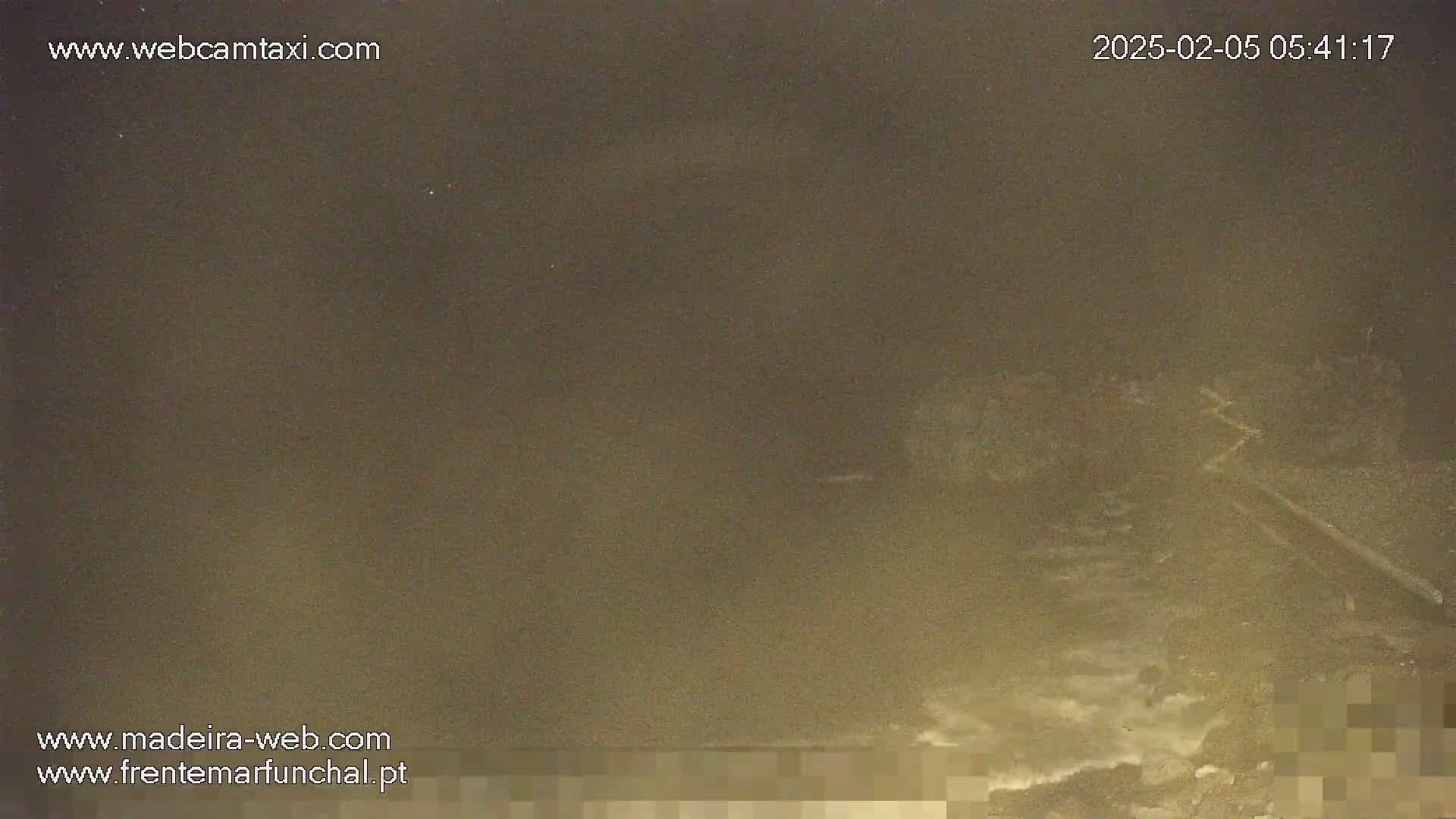 A blurry, nighttime image shows a dark, possibly foggy or hazy scene of an indistinct area near a body of water.