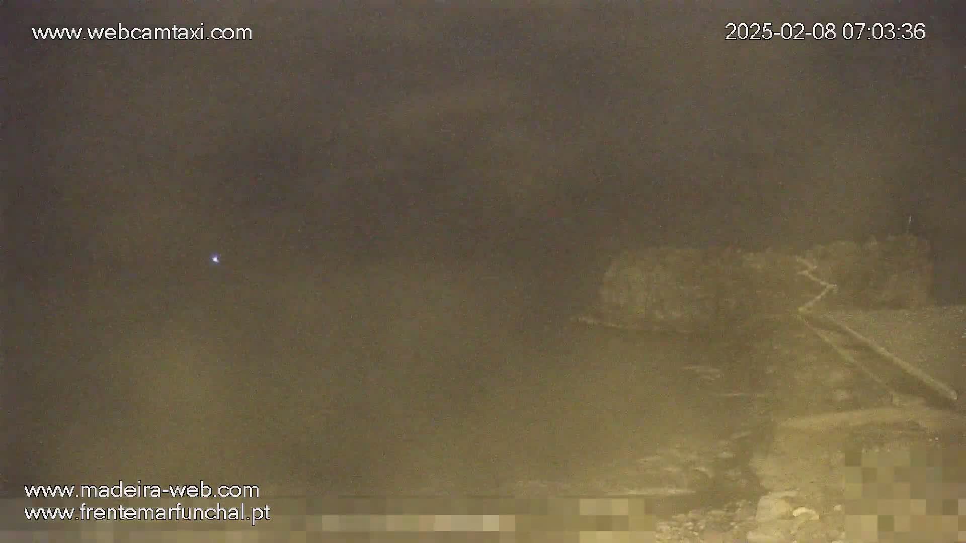 A nighttime, hazy view shows a dark, indistinct landscape with a small, bright light in the distance.