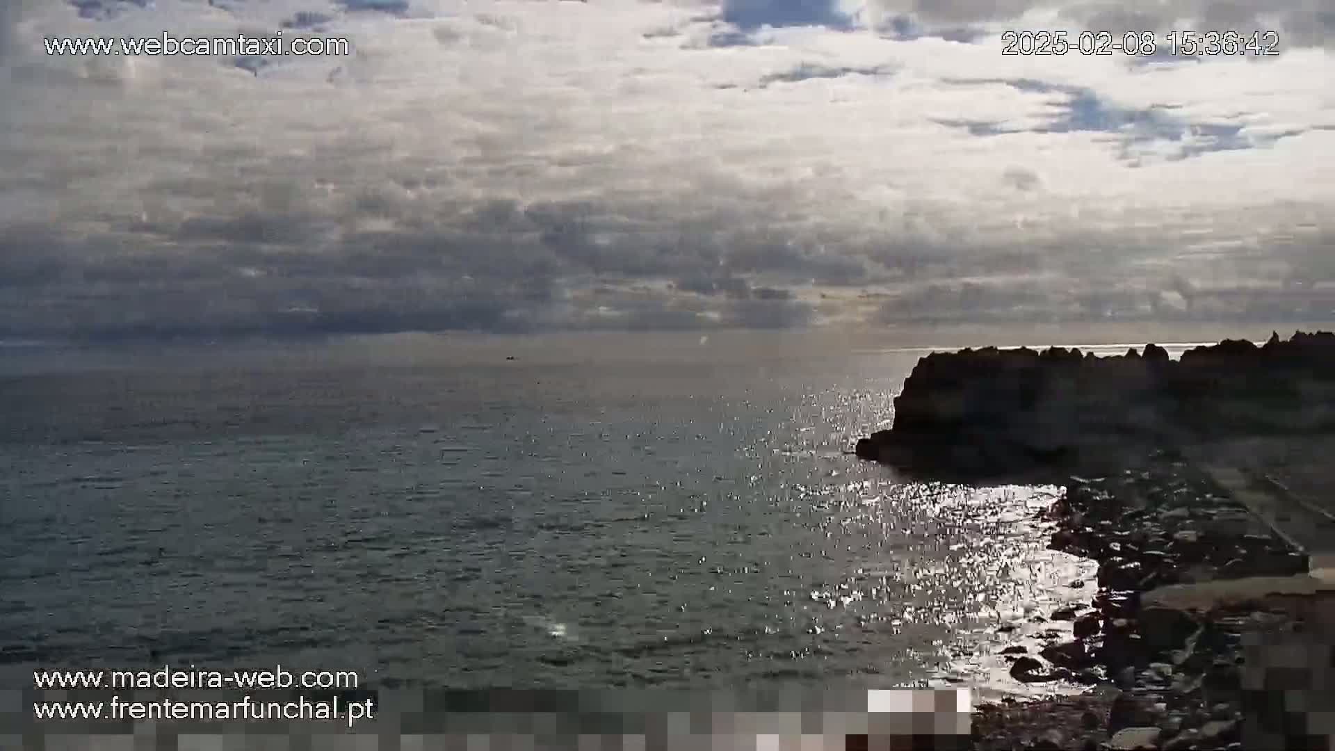 A partly cloudy sky overlooks a dark, calm ocean meeting a rocky shoreline.