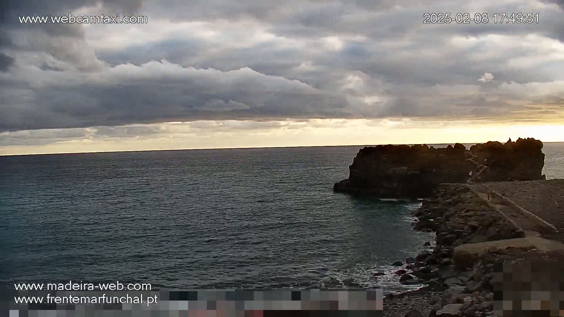 A dark, rocky outcropping juts into a calm ocean under a cloudy sky with a hint of sunset.