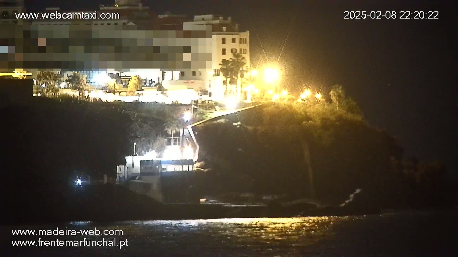 A nighttime, seaside view shows illuminated buildings on a cliff overlooking dark water.