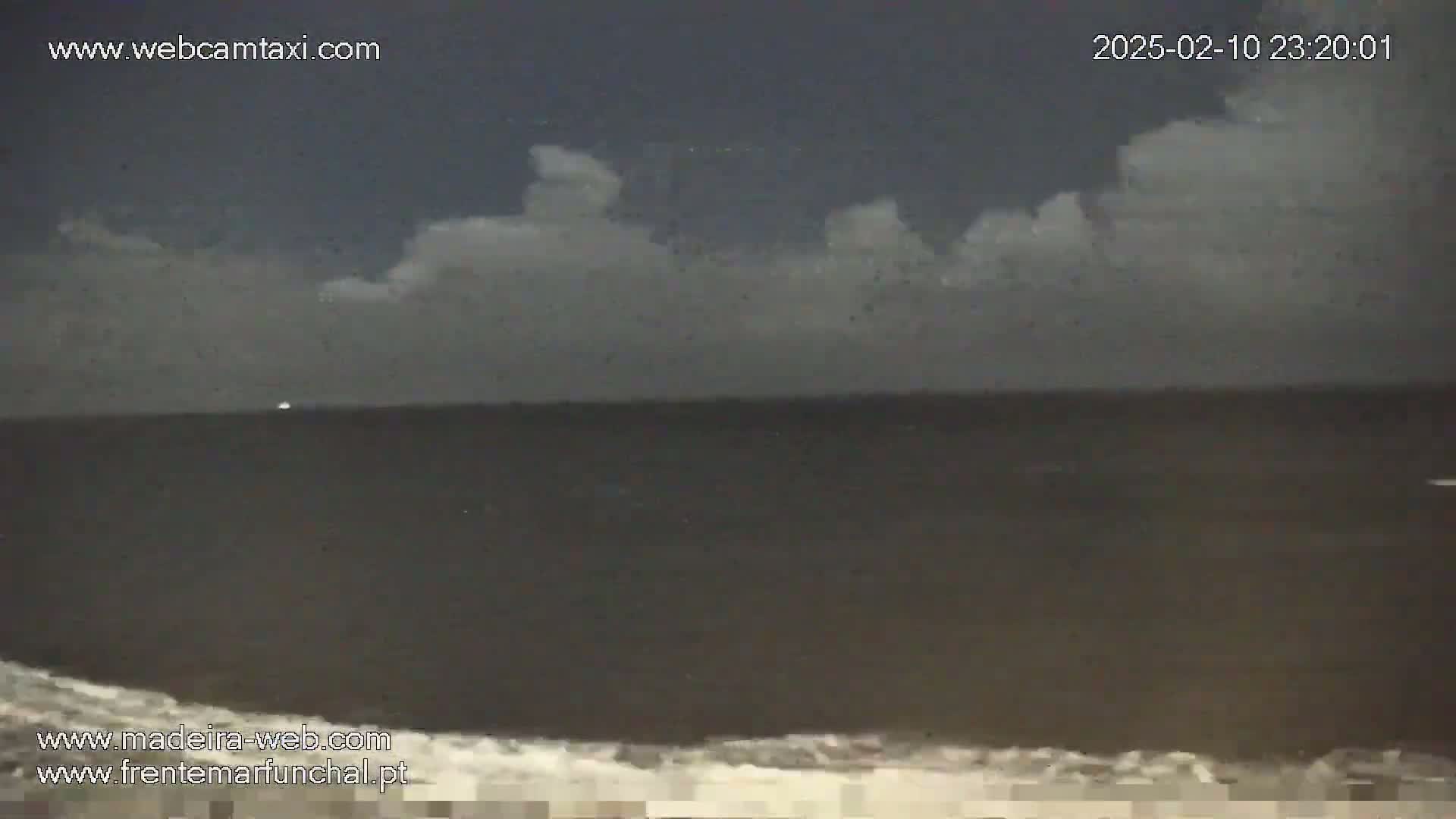 A dark ocean with a few small waves at the bottom is visible under a night sky with a layer of low clouds.