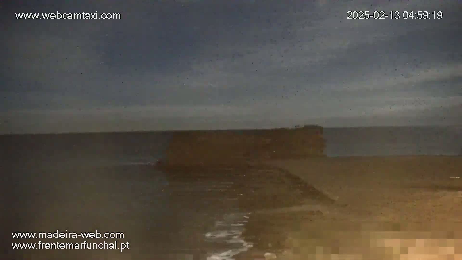 A dark, overcast sky hangs over a calm, dark-colored ocean meeting a sandy shore.