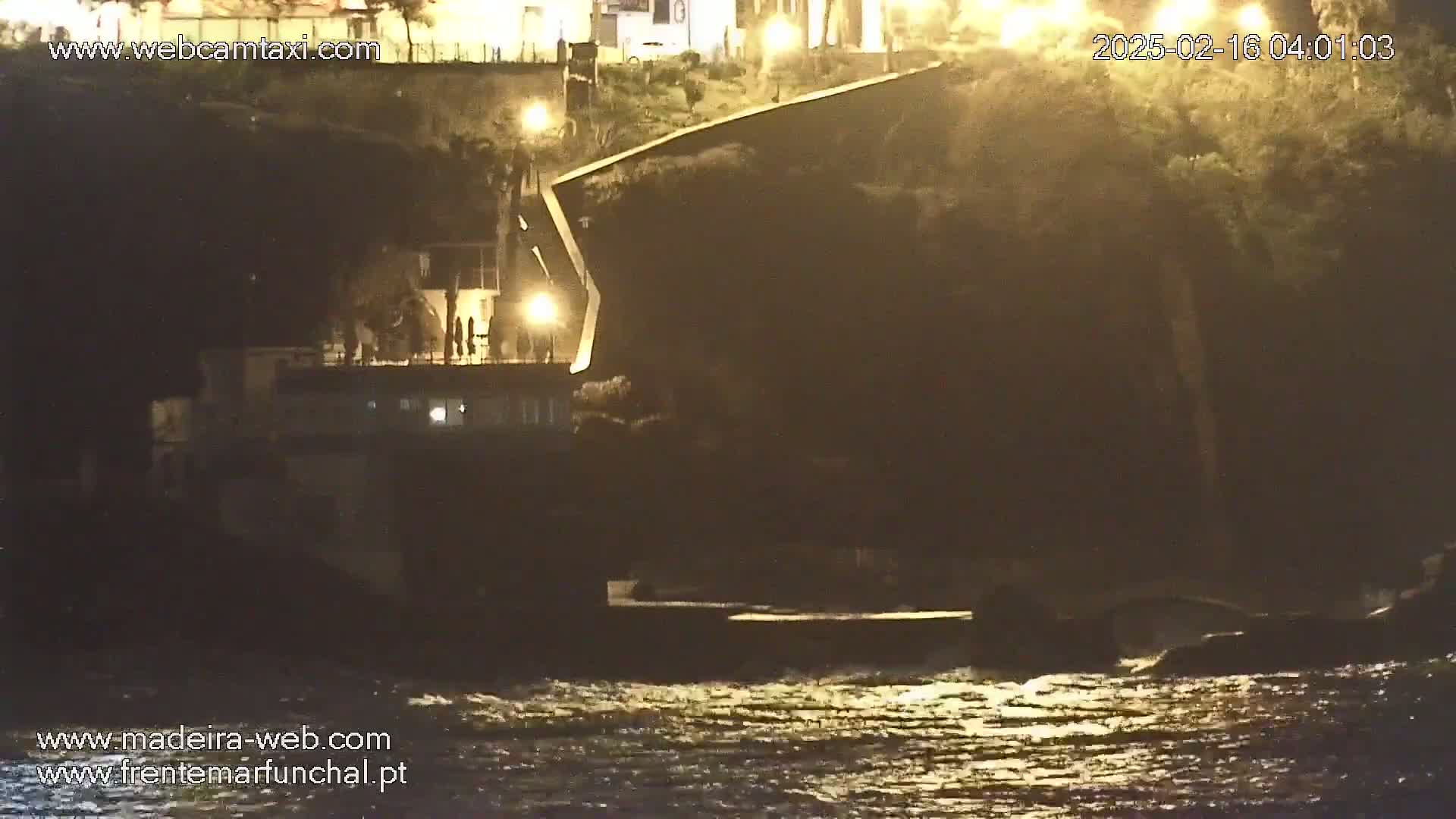 A dark, angular structure sits on a cliff overlooking a choppy nighttime ocean.