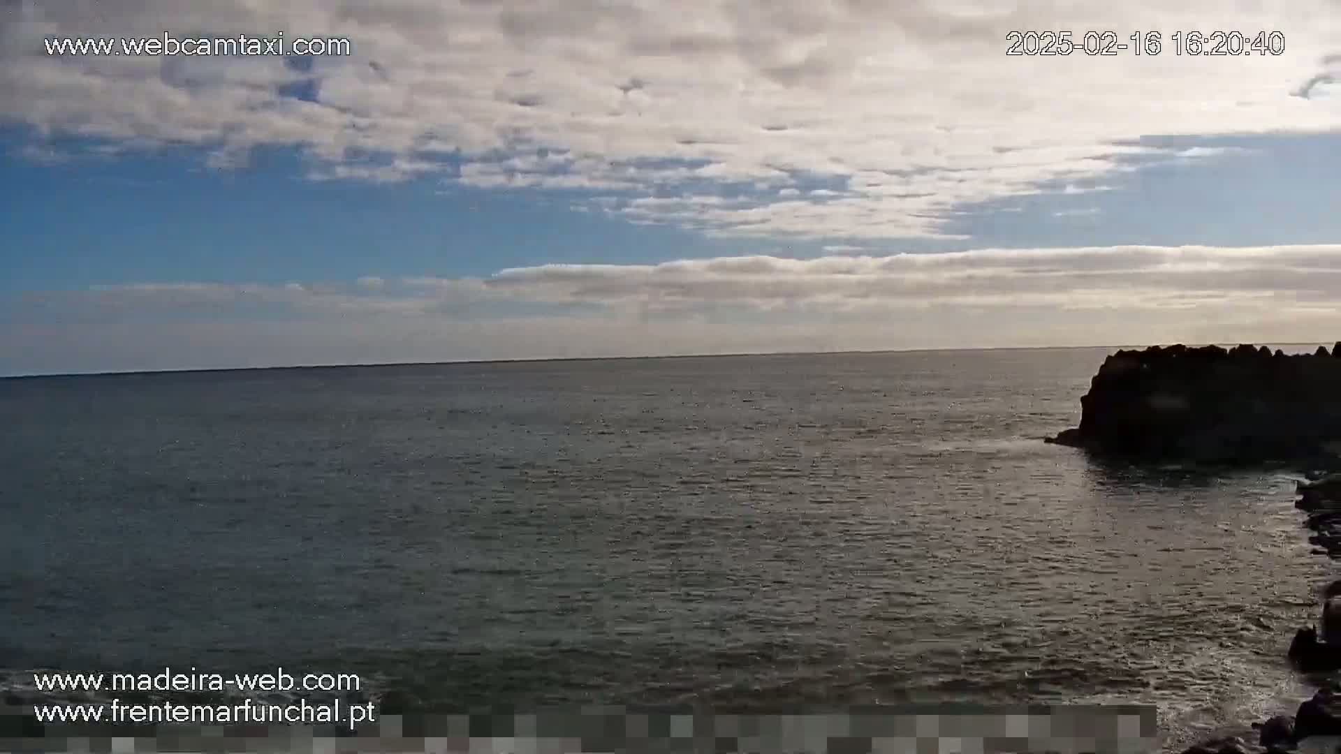 A partly cloudy sky overlooks a dark, somewhat choppy ocean meeting a rocky shoreline.