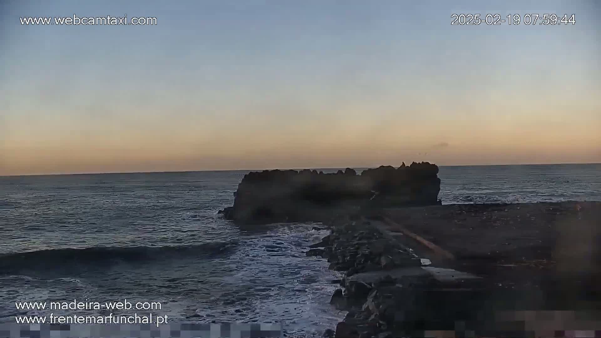 Dark, rocky shoreline meets a calm, dark ocean under a twilight sky.
