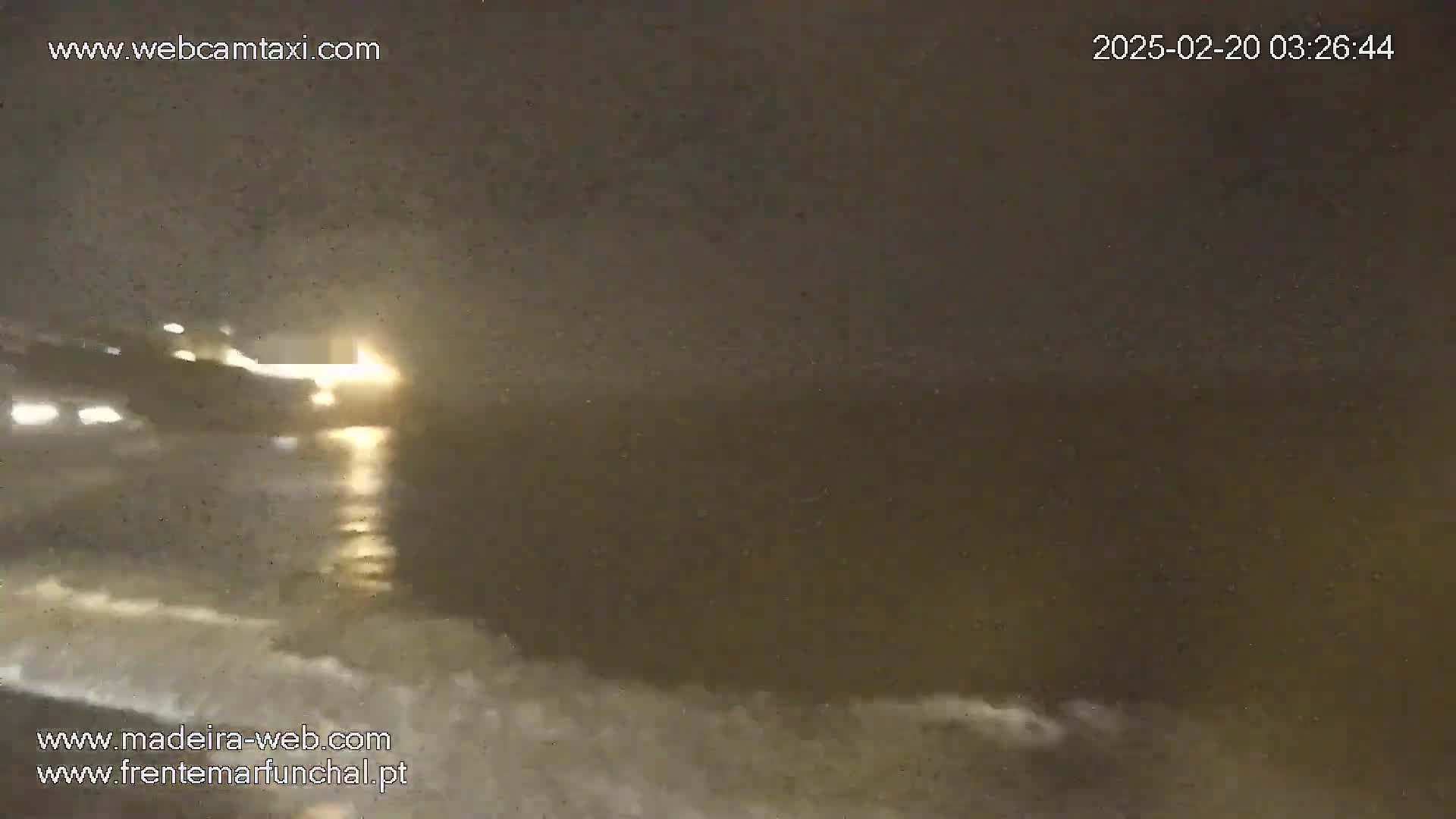 A nighttime view of a dark body of water with small waves, illuminated by bright lights in the distance.