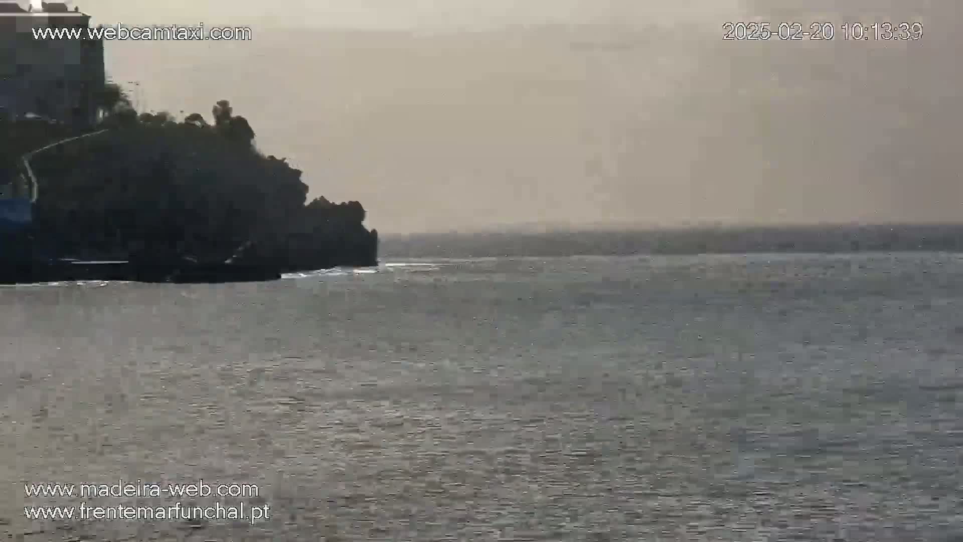 A hazy, overcast day reveals a dark rocky outcrop jutting into a choppy sea.