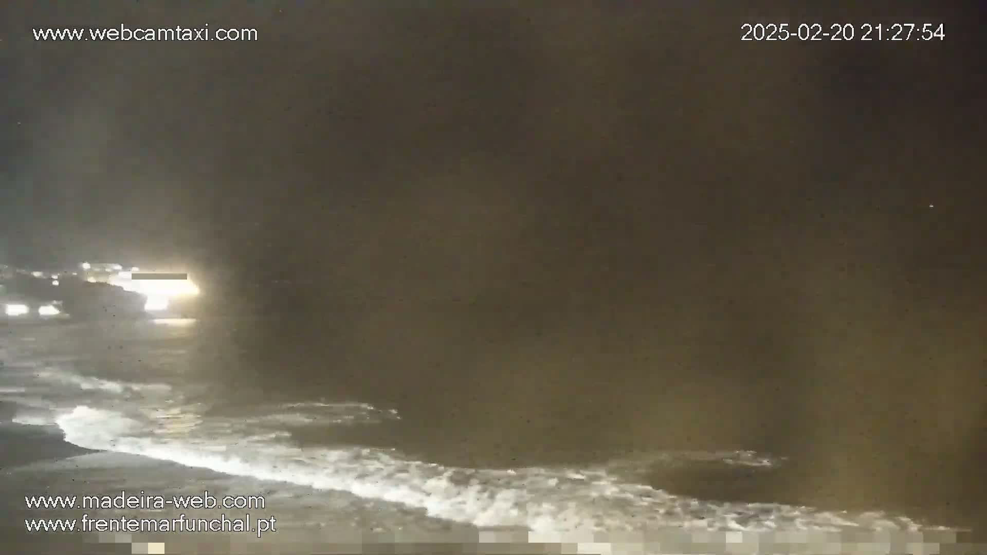 A dark, nighttime beach scene shows waves gently lapping the shore under an overcast sky.