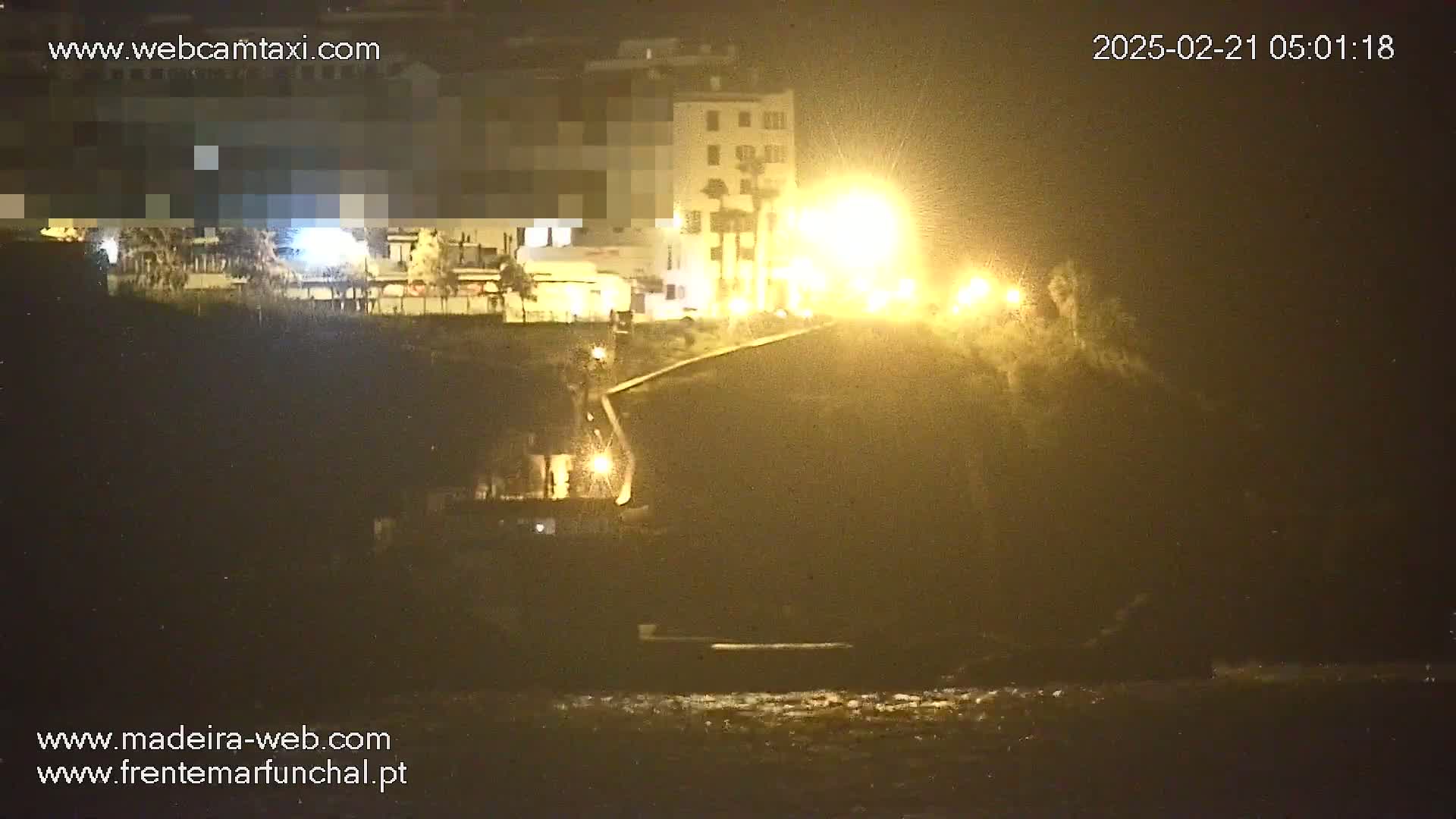 A nighttime coastal scene shows a dark clifftop with buildings illuminated by streetlights, overlooking a dark body of water.