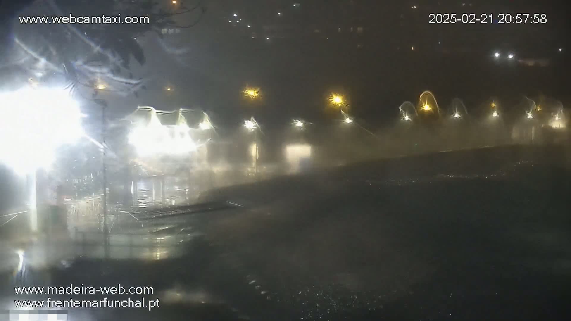 A nighttime scene shows a row of buildings illuminated by lights in heavy rain and wind.