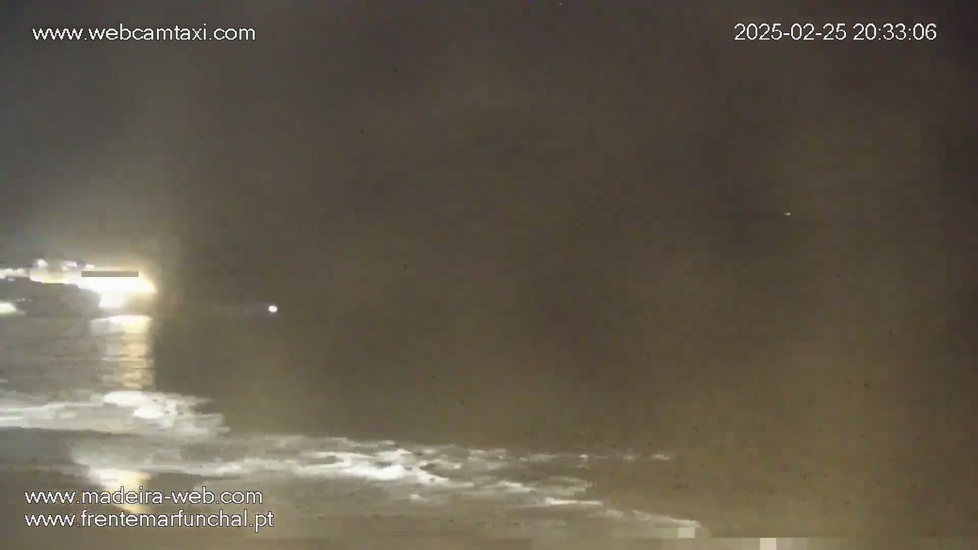 A nighttime coastal scene shows dark, slightly wavy water under a hazy, dark sky with a bright light source visible on the left.