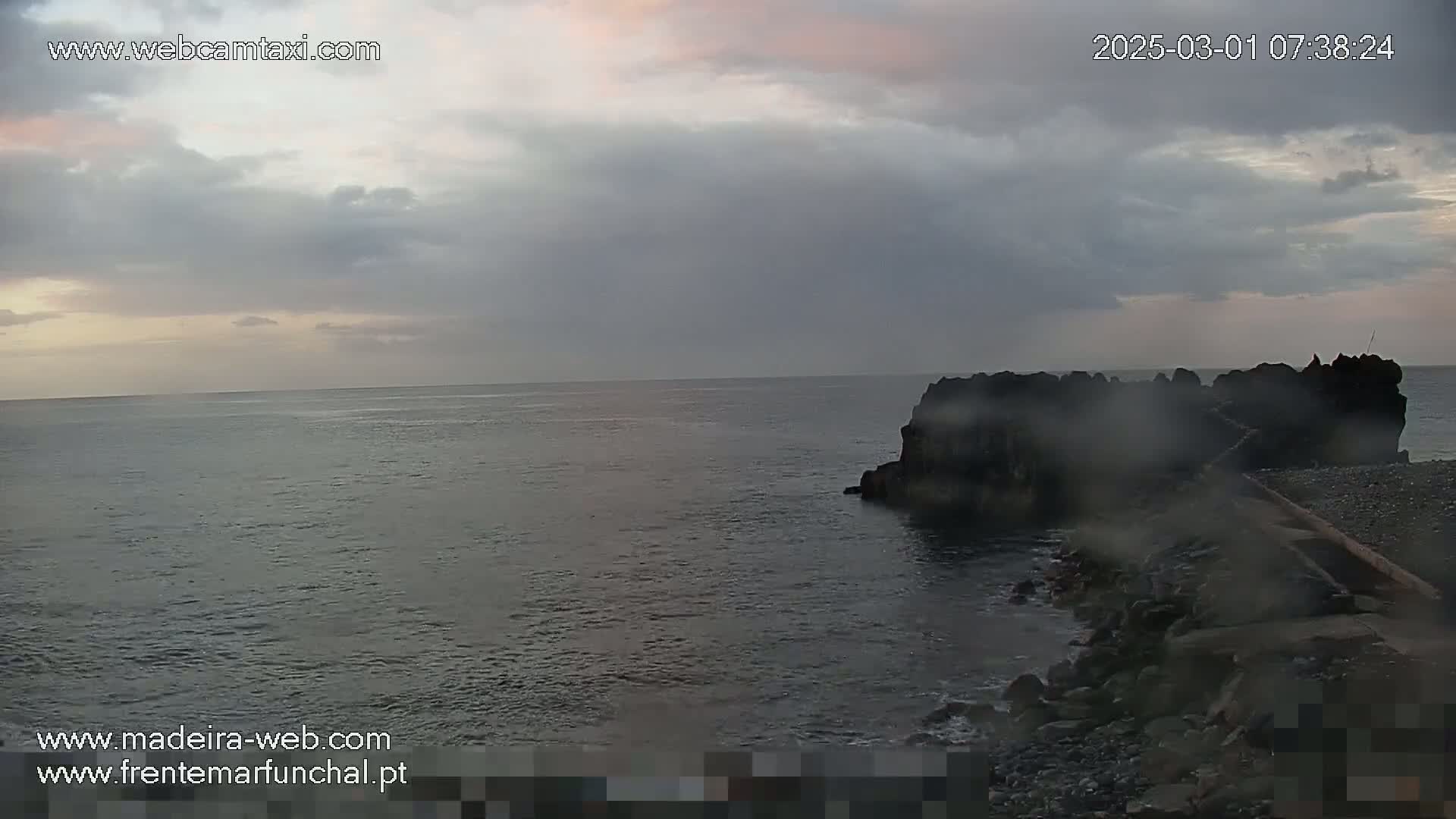 A dark, rocky outcropping juts into a calm, gray ocean under an overcast sky.