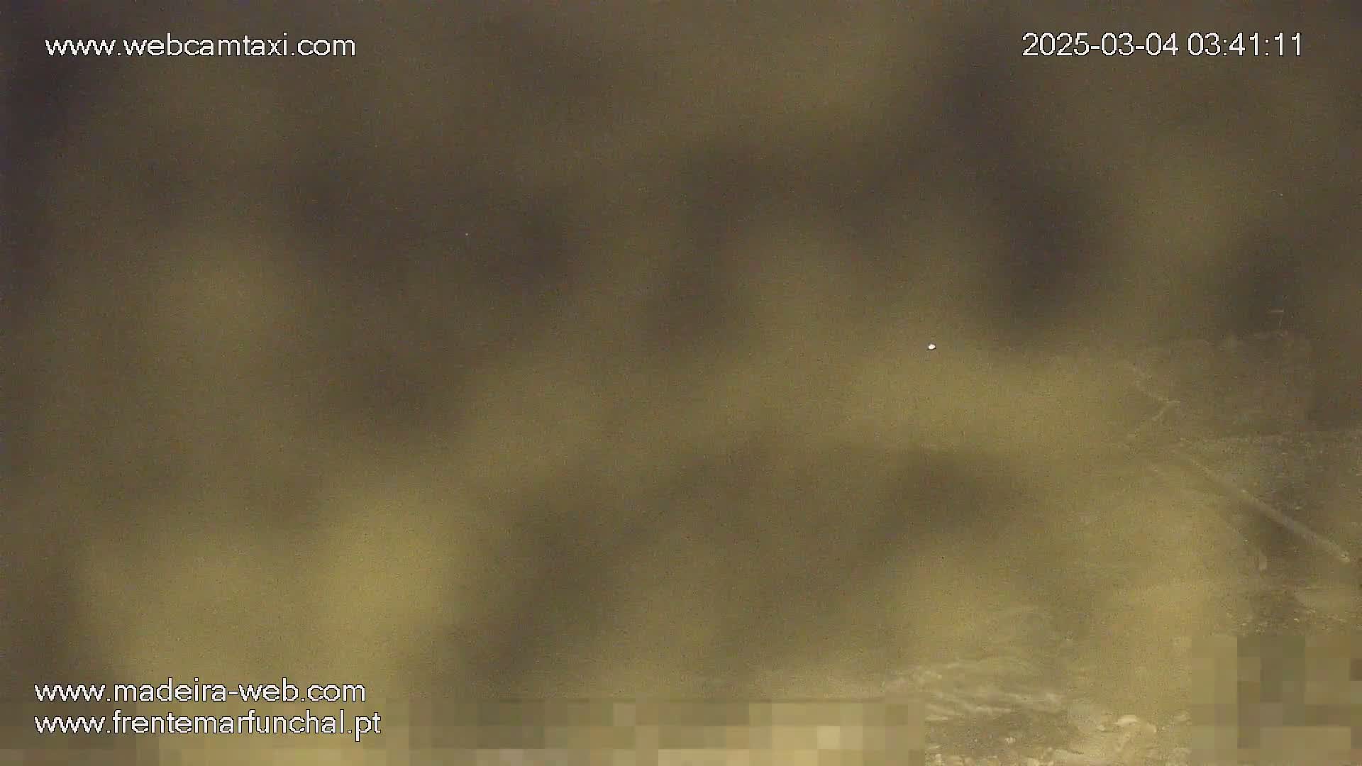 A nighttime, hazy, blurry view of a dark body of water with indistinct shoreline.