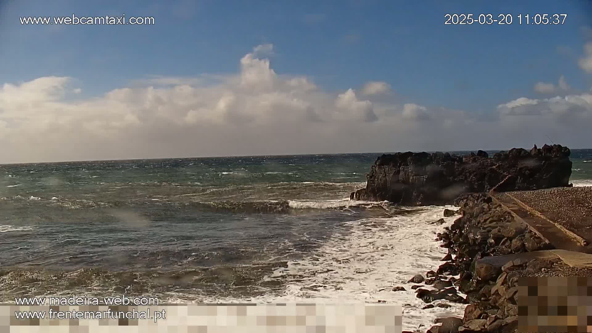 A rocky outcrop juts into a choppy sea under a partly cloudy sky.