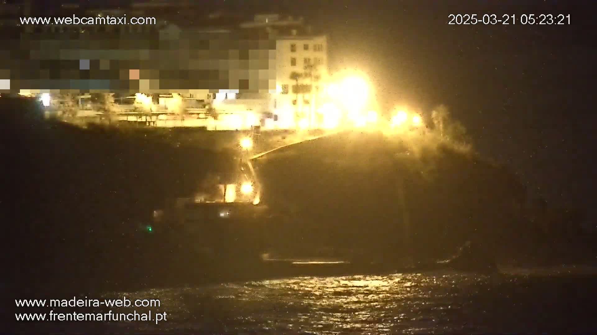 A nighttime, rain-swept coastal scene shows brightly lit buildings overlooking a dark, choppy ocean.