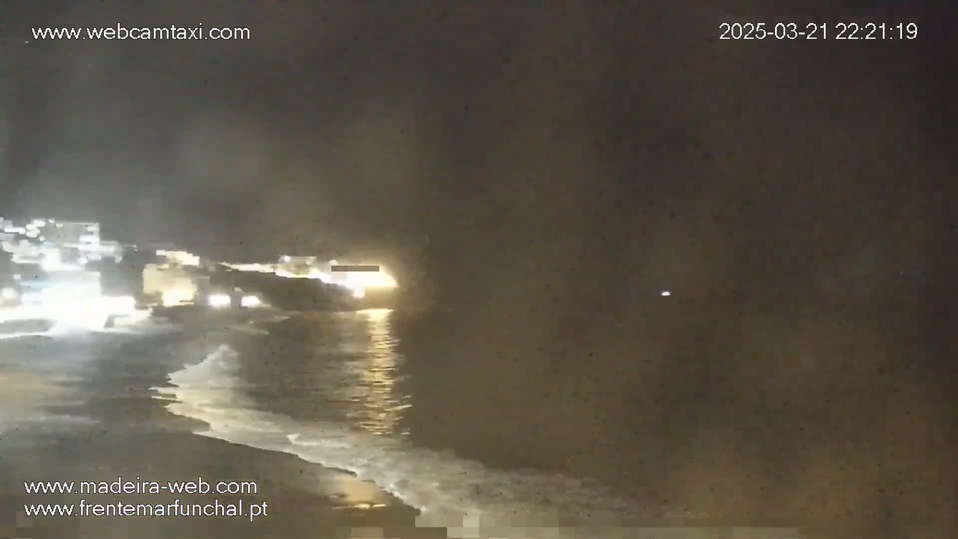 A nighttime view shows a dark, sandy beach with gentle waves lapping the shore under a hazy, dark sky.