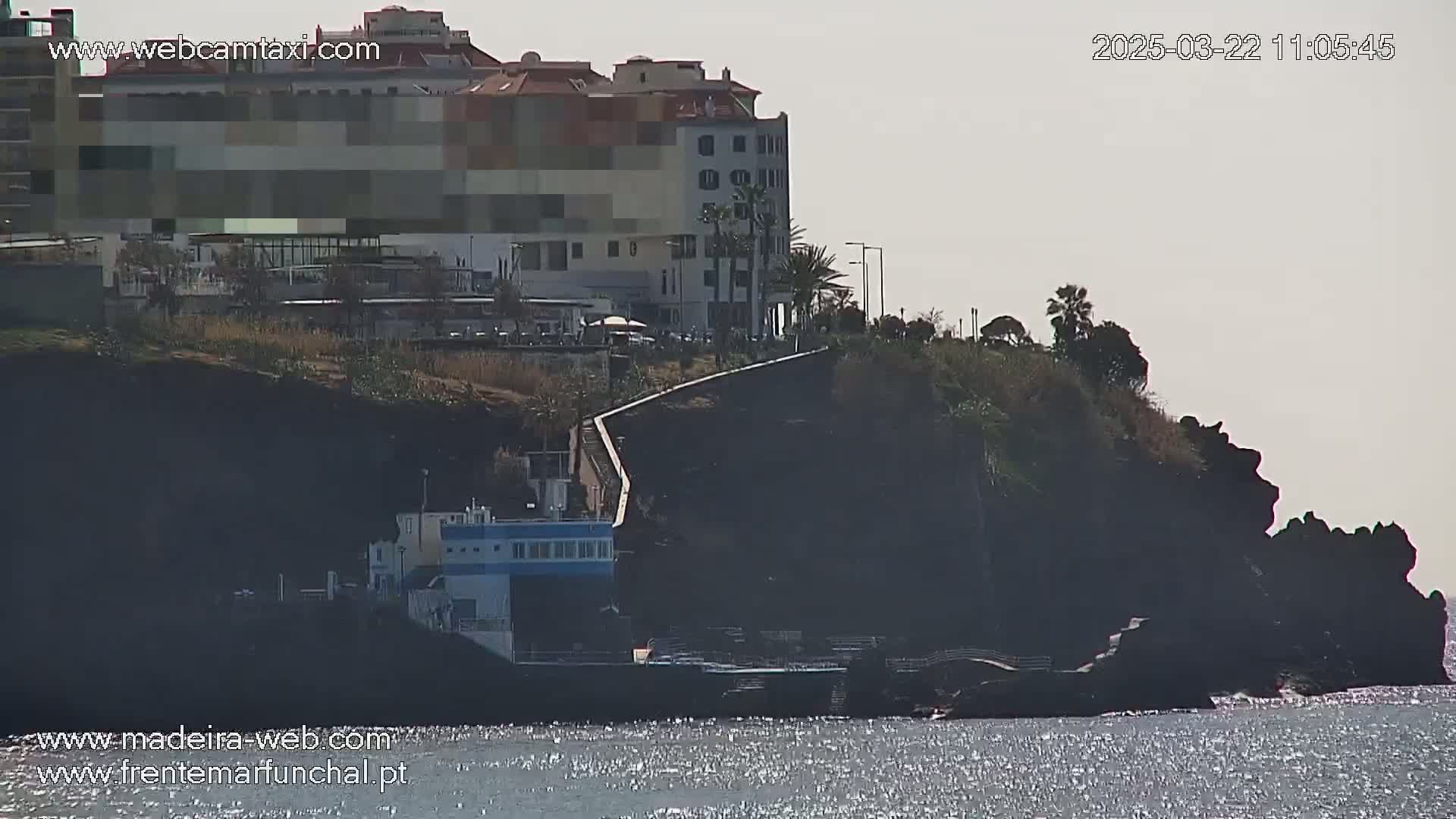 A multi-story building is situated on a cliff overlooking a calm body of water under a hazy sky.