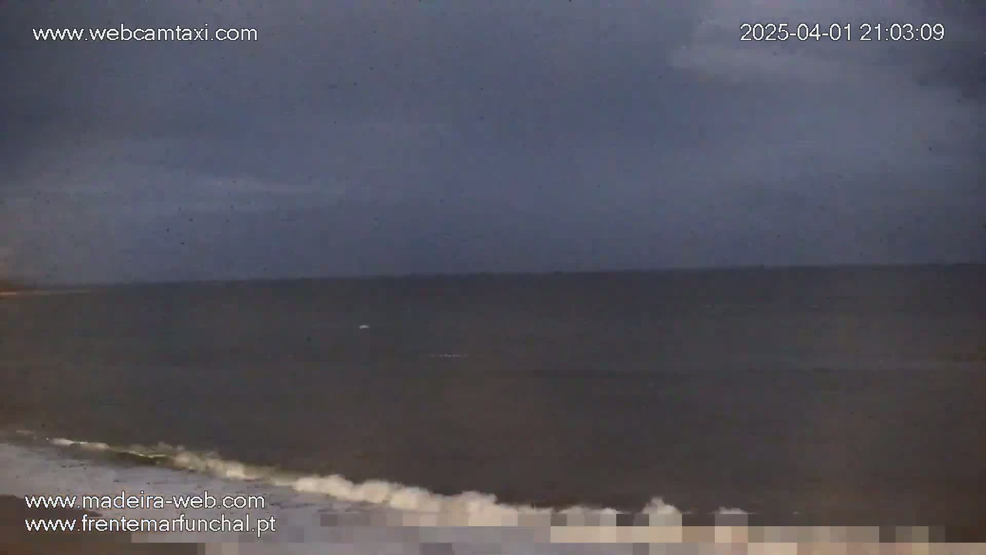 A dark, overcast sky hangs over a calm, gray ocean with small waves breaking on the shore.