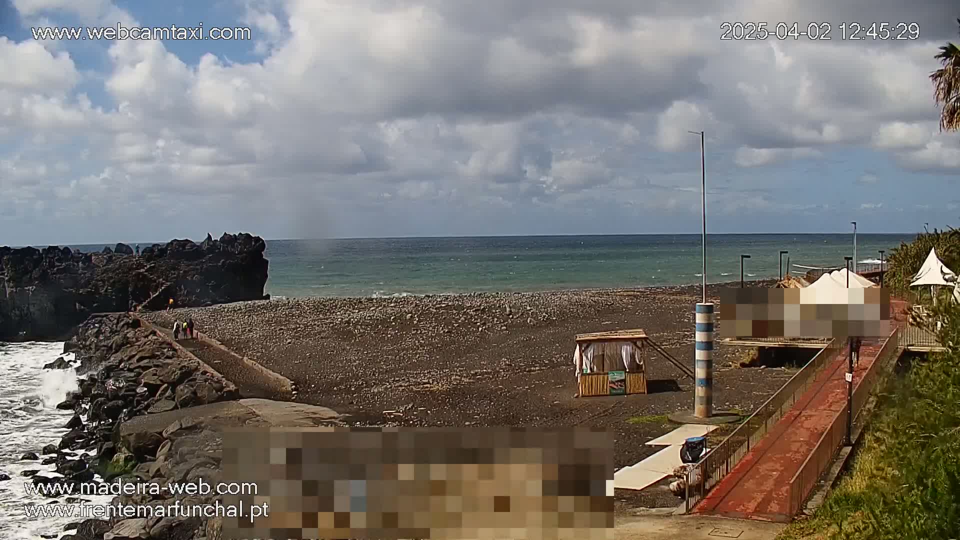 A rocky shoreline with a dark-colored beach stretches to a calm ocean under a partly cloudy sky.