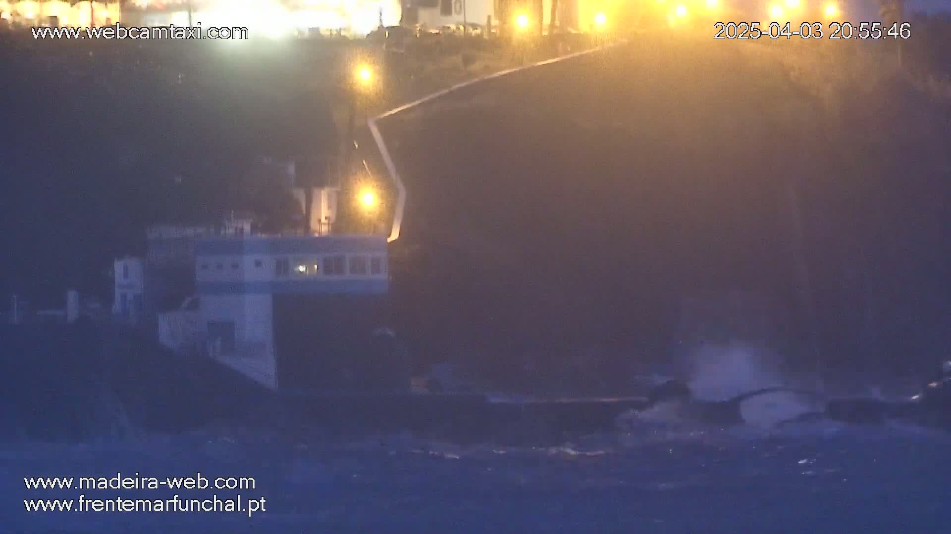 A boat is partially visible near a dark cliff at night in rough, stormy water.