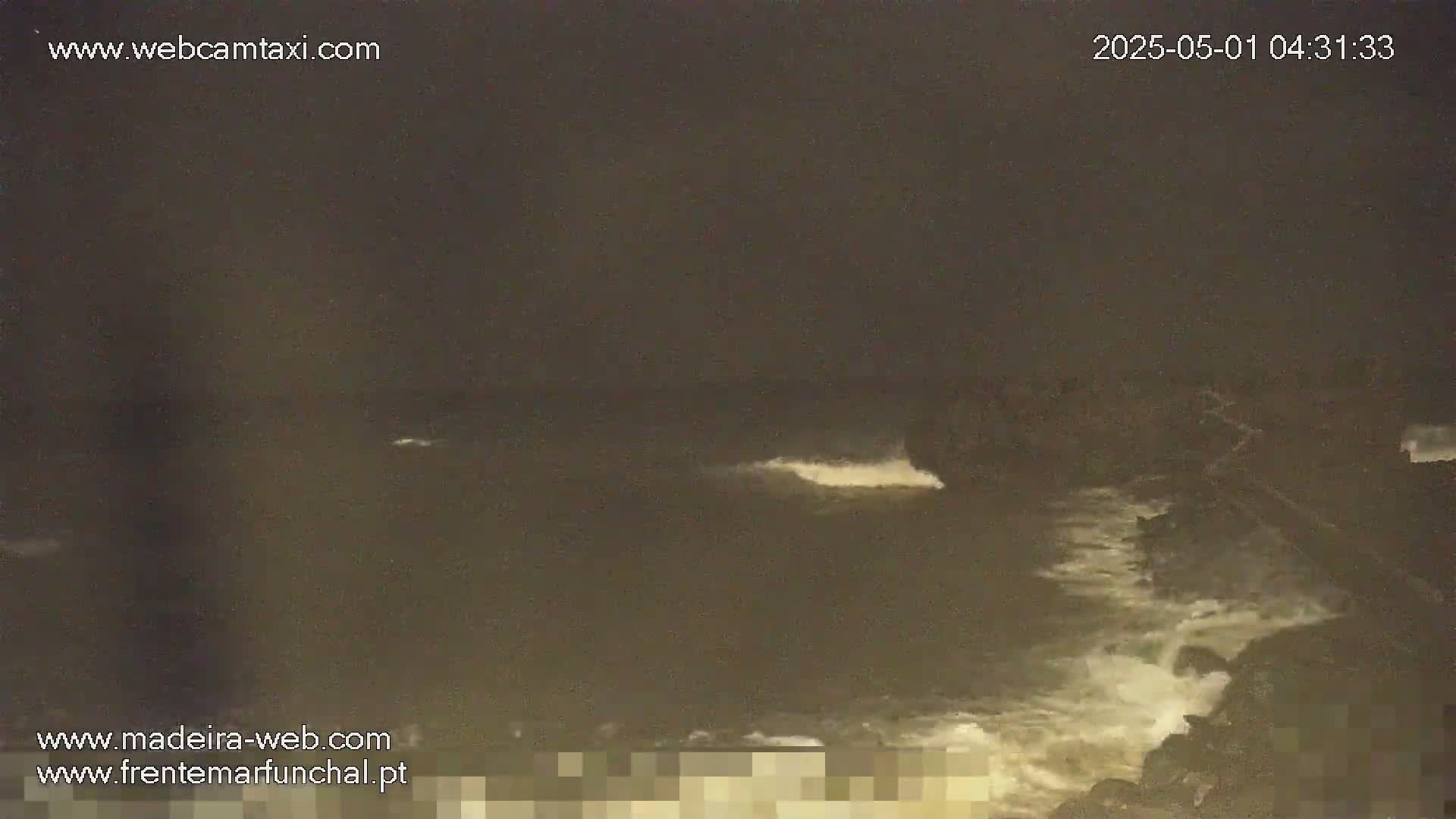 A dark, nighttime ocean scene shows waves crashing against a rocky shore under a cloudy sky.
