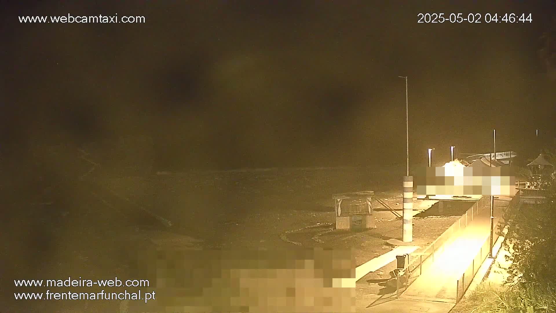 A nighttime view of a beach area with a pathway leading to a structure near the water, under dark, overcast conditions.