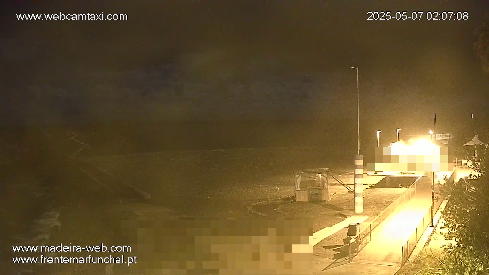 A nighttime view of a dark, somewhat stormy beach with a dimly lit walkway and building.