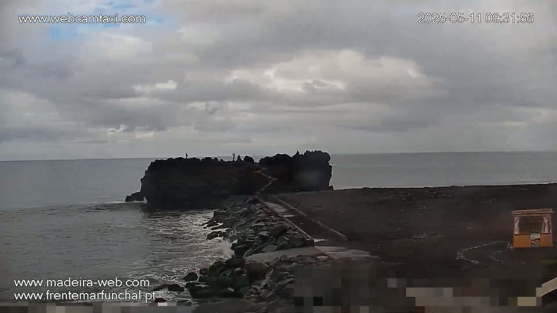 A rocky outcropping juts into a dark ocean under a cloudy sky.