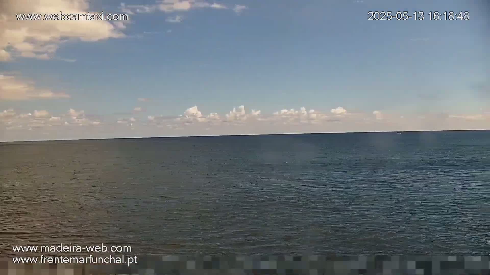 A calm ocean stretches to a horizon under a mostly clear sky with a few scattered clouds.