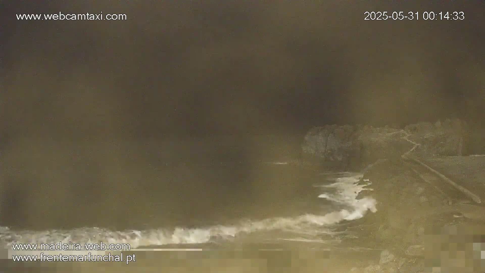 Dark, nighttime waves crash on a rocky shore.