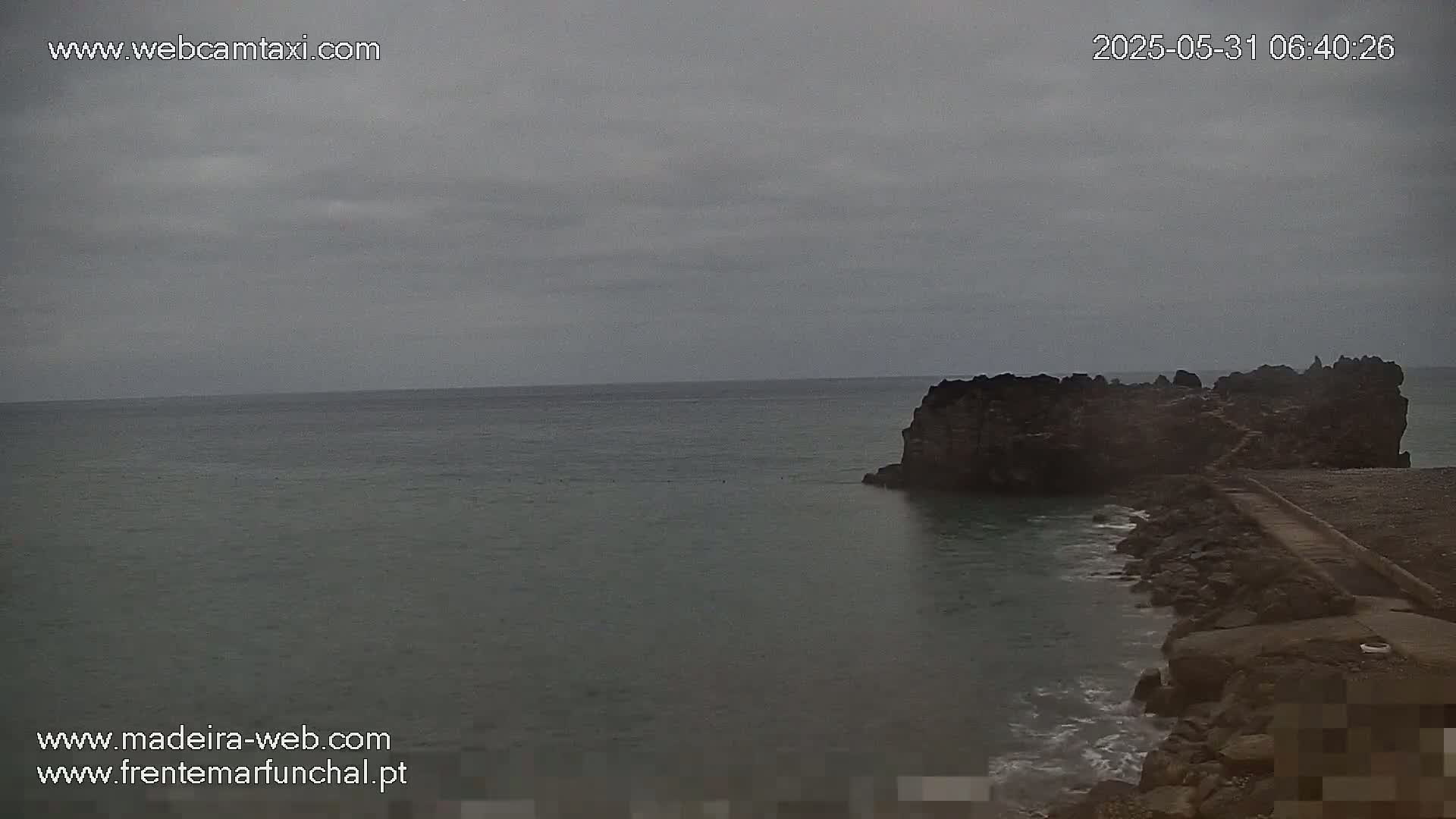 A rocky outcropping juts into a calm, grey sea under an overcast sky.