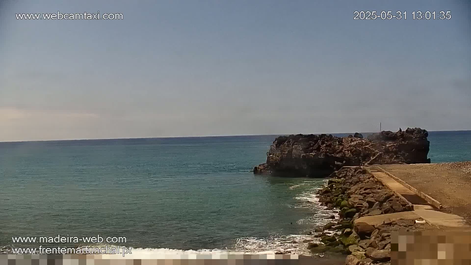 A rocky outcrop juts into a calm, teal ocean under a clear sky.