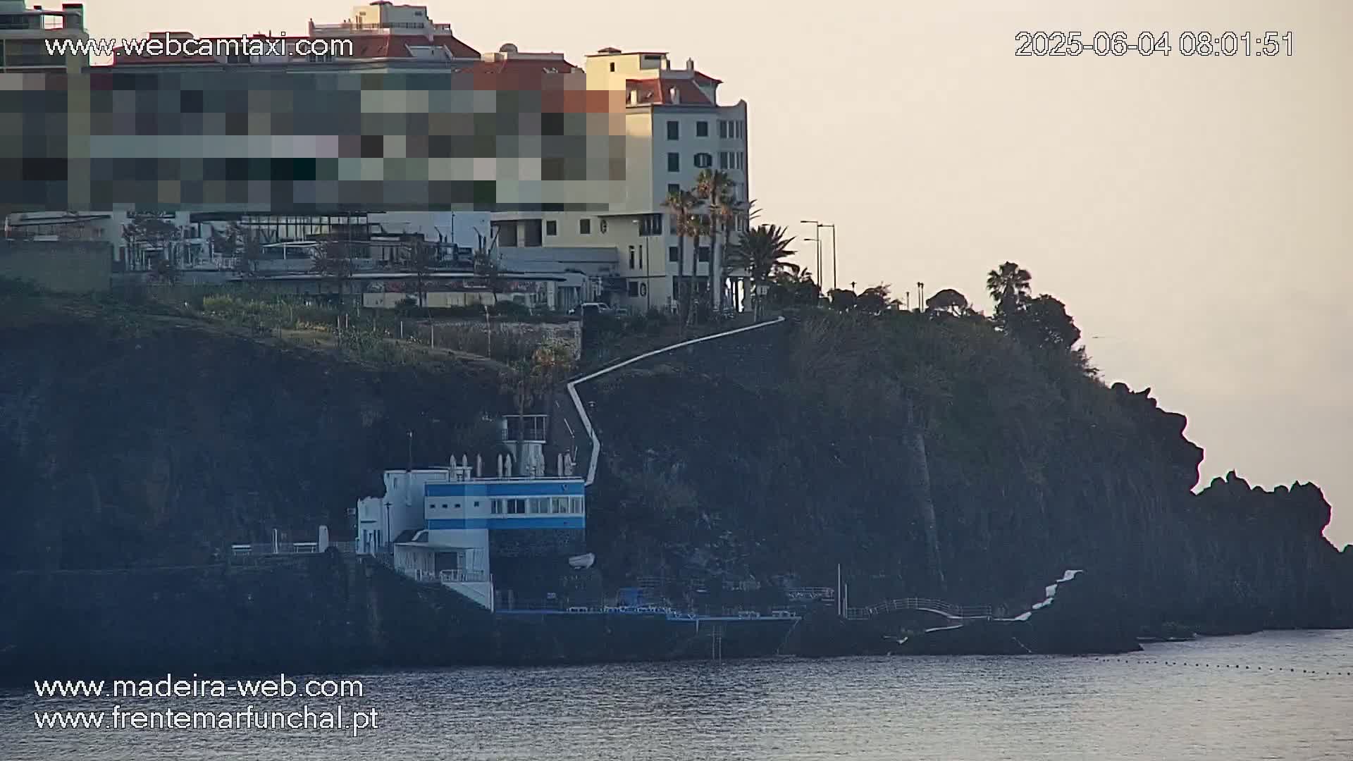 A coastal scene at dawn shows a building on a cliff overlooking the ocean, with a path leading down to a smaller structure near the water.