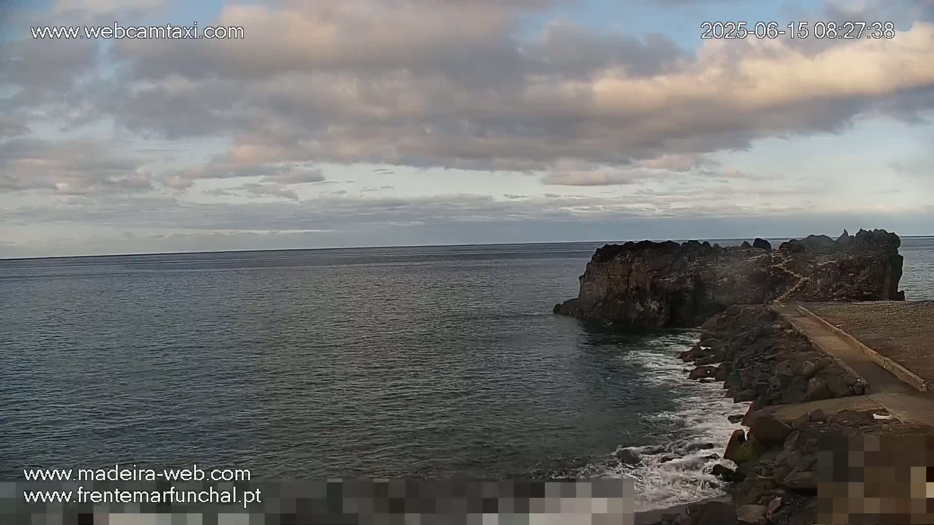 A rocky outcrop juts into a dark-green ocean under a partly cloudy sky.