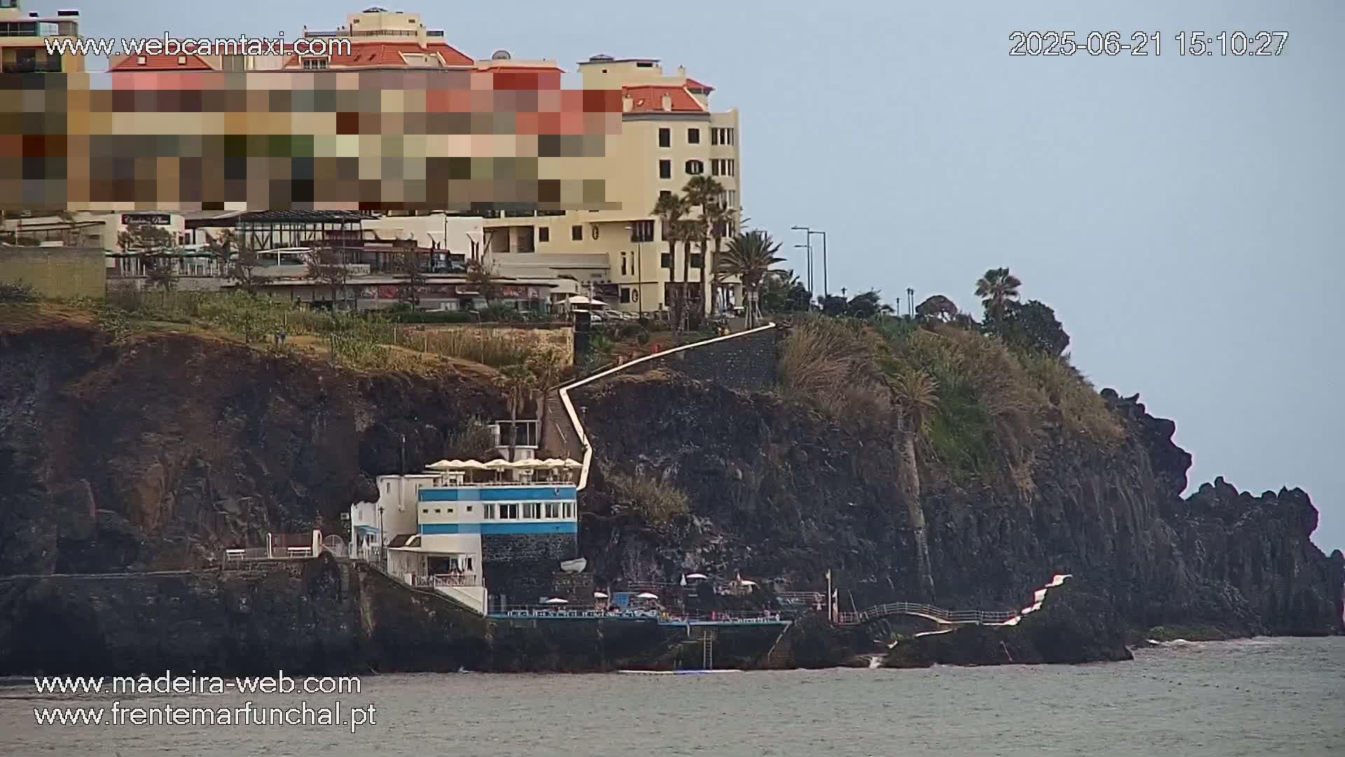 A coastal scene shows a multi-story building overlooking dark cliffs and the ocean under an overcast sky.