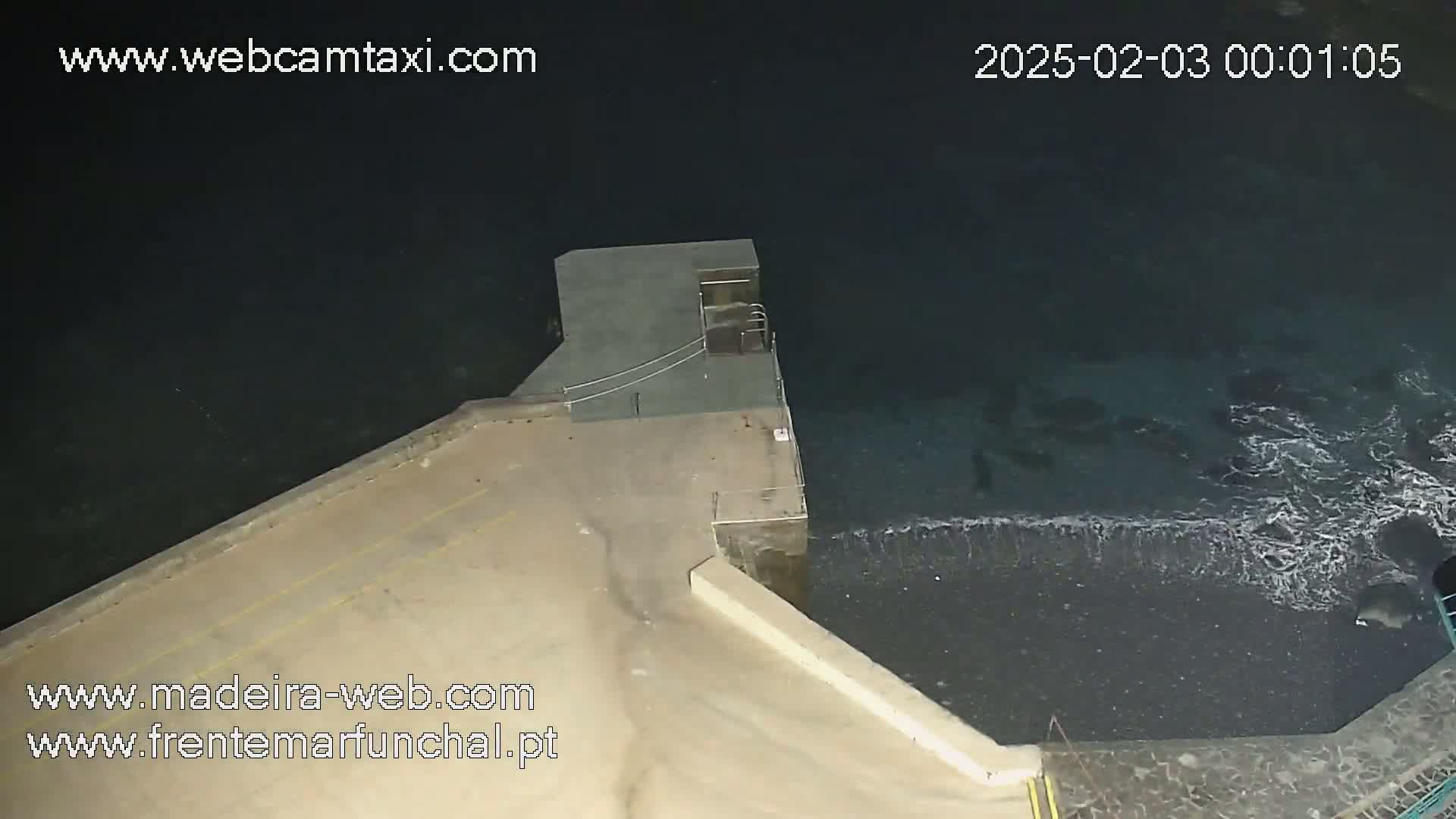 A nighttime overhead view shows a concrete platform extending into dark ocean water with small waves lapping at the edge.