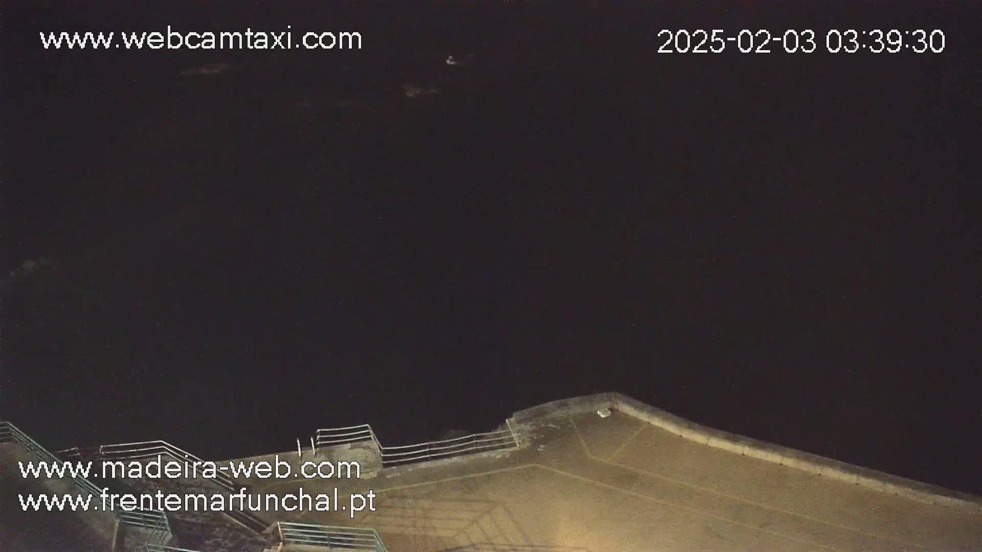 A dark nighttime scene shows a concrete wall extending into a very dark body of water.