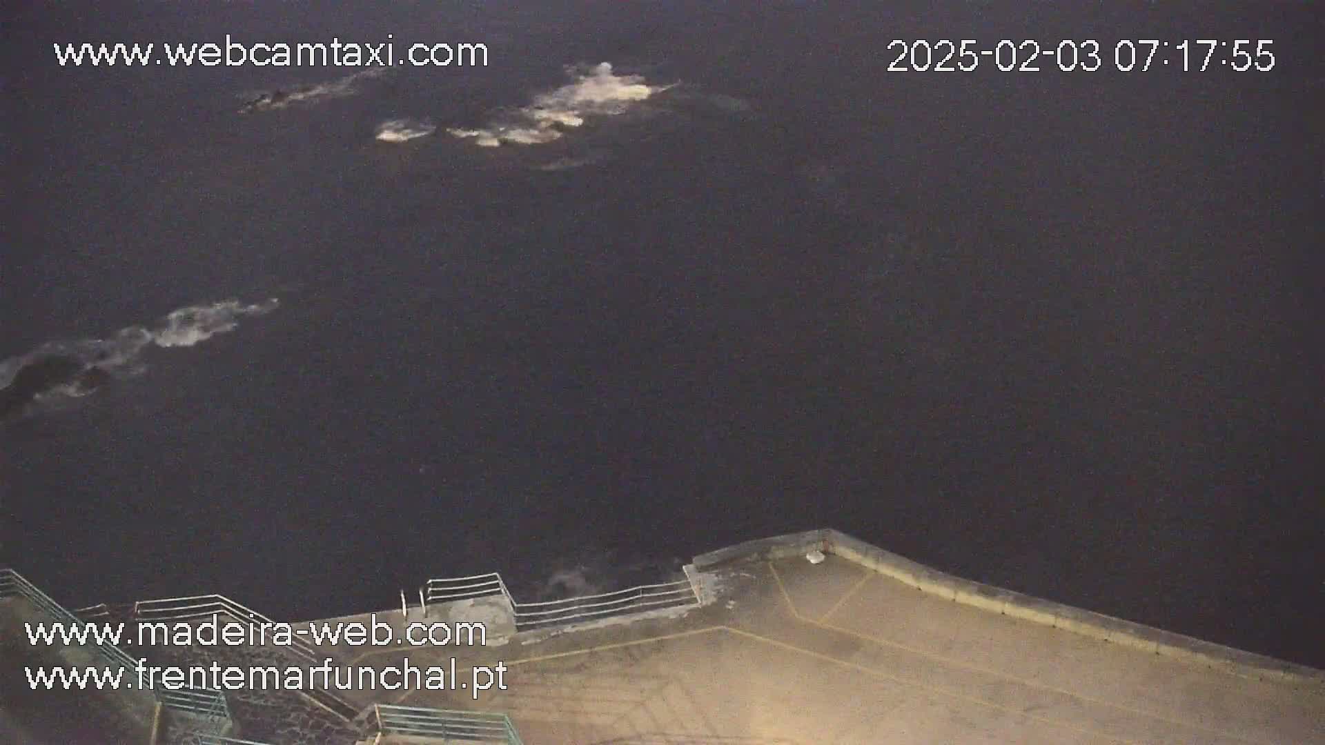 A nighttime view of dark water with some whitecaps near a concrete wall.
