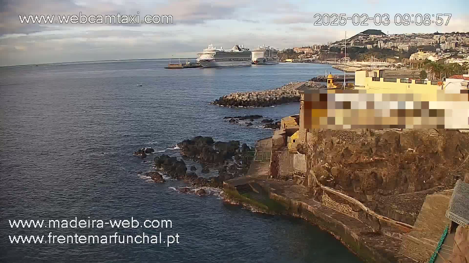 Two cruise ships are docked in a harbor near a rocky shoreline under a partly cloudy sky.
